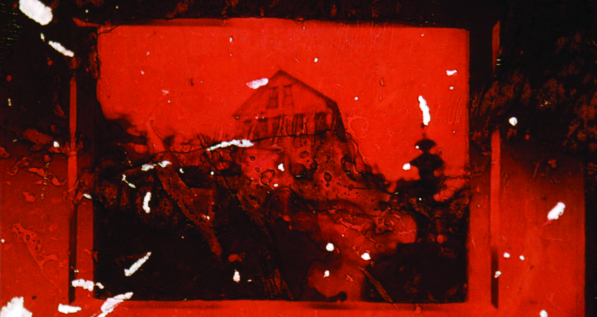 Image couleur flou, en noir et orange. Une maison en arrière plan. De la pellicule brûlée et grattée en premier plan