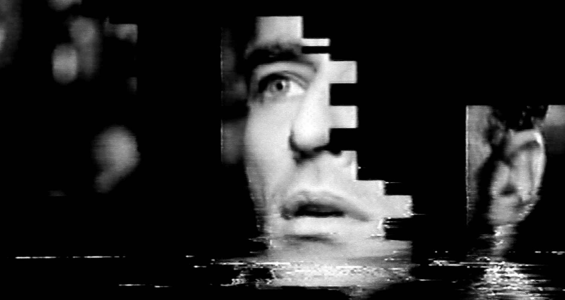 Black and white video image. A man's face is cut into pieces