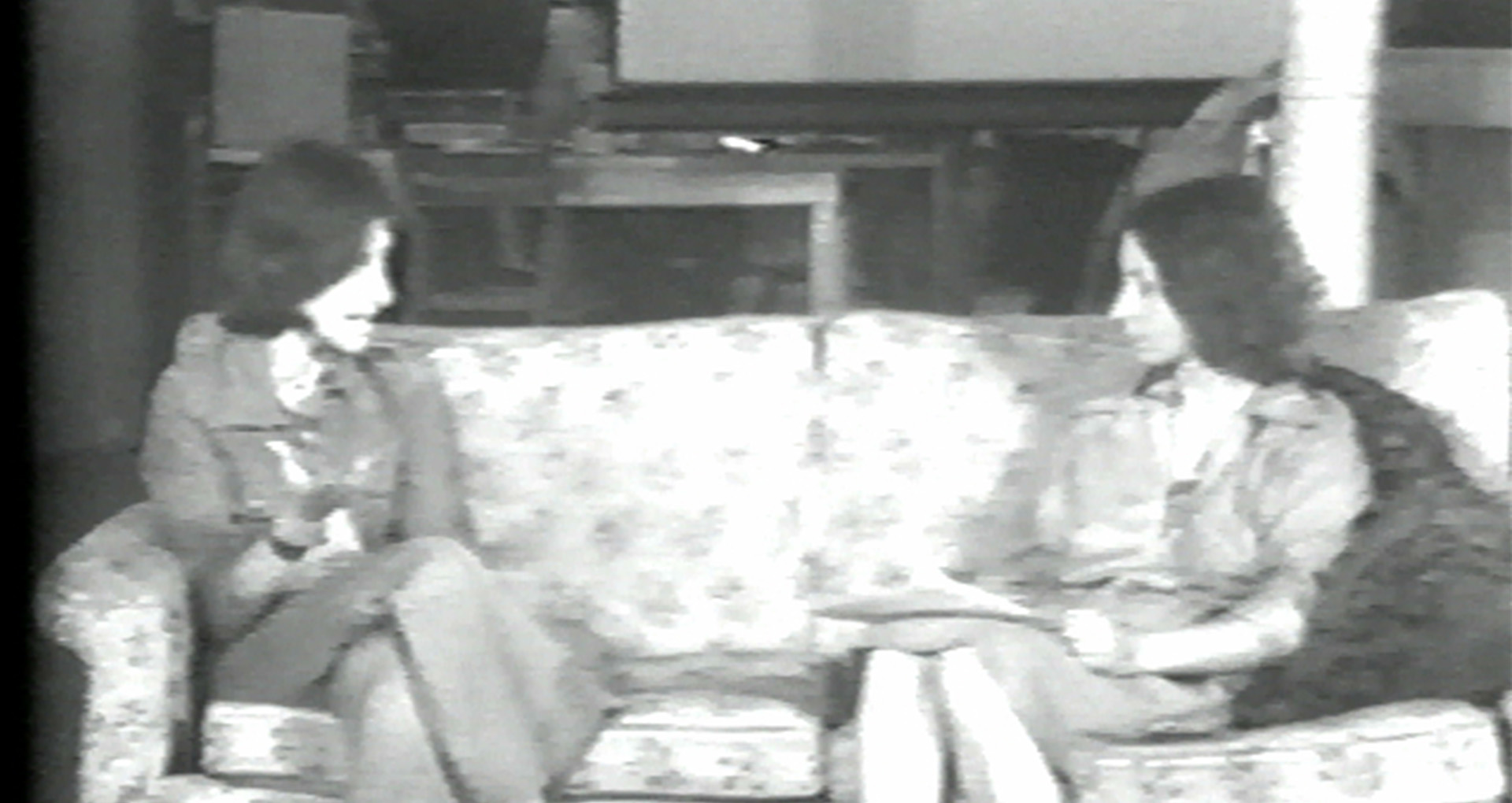 Black and white video still. 2 women sitting on a couch